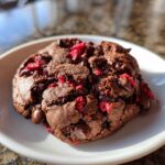 A close-up of a rich, dark chocolate cherry cookies, studded with chocolate chips and bright red dried cherries.