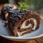 Close-up of a slice of chocolate yule log cake showing the dark chocolate frosting texture and white cream swirl filling.
