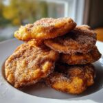 A close-up stack of golden brown, freshly fried buñuelos heavily coated in cinnamon sugar.