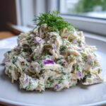 A mound of creamy cottage cheese chicken salad mixed with red onion and topped with fresh dill.