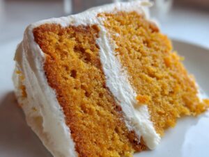 Close-up of a moist slice of orange Creamsicle Cake layered with thick white frosting.