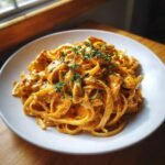 A close-up of creamy cajun chicken pasta with fettuccine noodles and chopped parsley garnish.