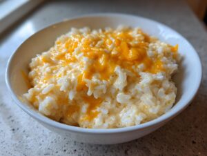Close-up of creamy cheesy rice topped with melted cheddar cheese, served in a white bowl.