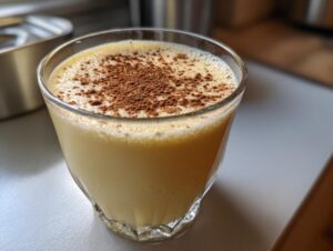 Close-up of a glass filled with creamy, yellow eggnog topped generously with ground cinnamon.