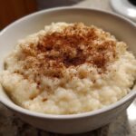Close-up of a white bowl filled with creamy rice pudding generously dusted with ground cinnamon.