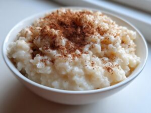 Close-up of a white bowl filled with creamy rice pudding generously topped with ground cinnamon.