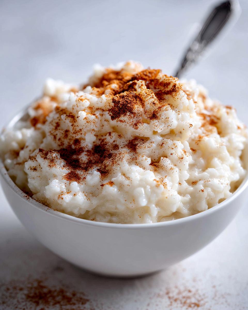 Close-up of creamy rice pudding in a white bowl, generously sprinkled with ground cinnamon.