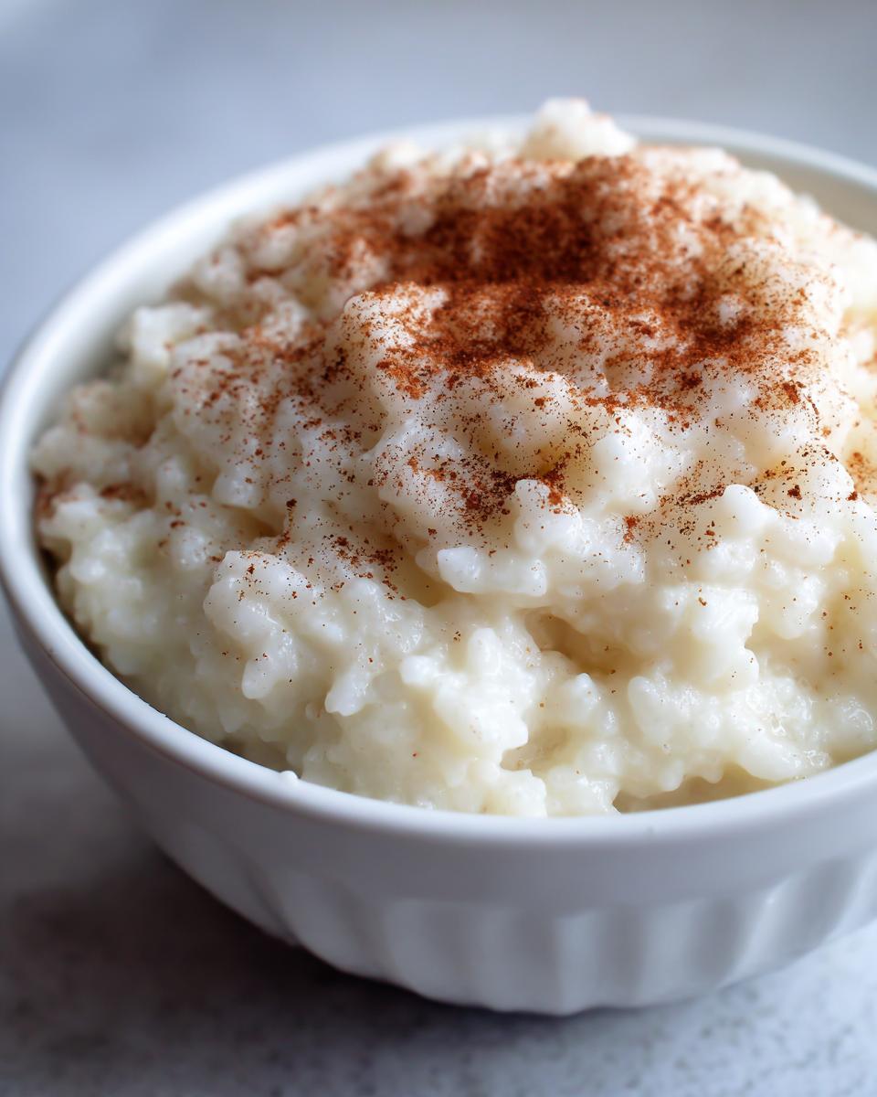 Close-up of creamy rice pudding in a white bowl, generously sprinkled with ground cinnamon.
