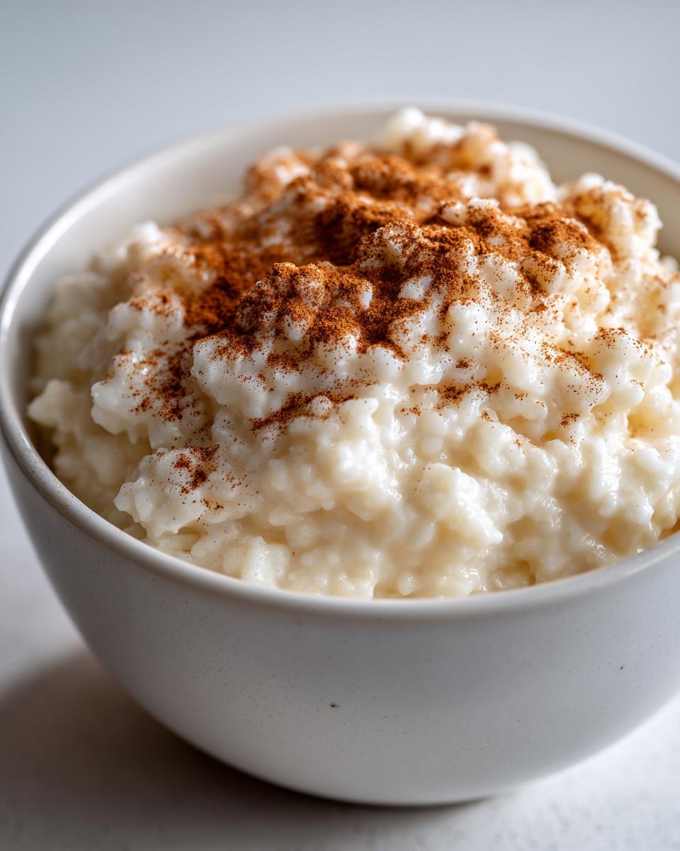 Close-up of creamy rice pudding topped generously with ground cinnamon in a simple white bowl.