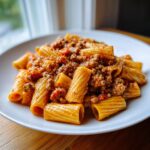 A close-up of creamy sausage pasta made with rigatoni tubes, served on a white plate.