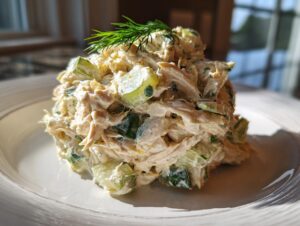 A mound of creamy dill pickle chicken salad featuring shredded chicken and chopped pickles, garnished with fresh dill.
