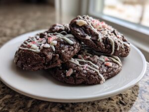 A stack of rich, dark double chocolate peppermint cookies drizzled with white icing and topped with crushed candy canes.