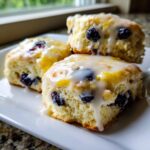 Three fluffy lemon blueberry scones topped with a thick, dripping lemon glaze, showcasing visible blueberries.