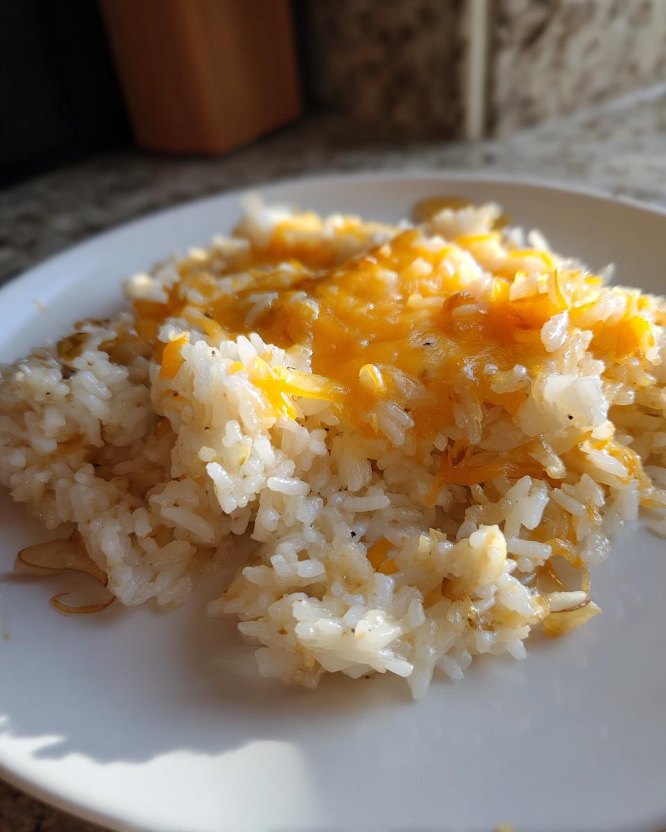 A close-up of fluffy white rice topped with melted orange cheddar cheese, representing french onion butter rice.