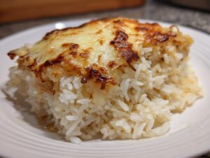 A close-up serving of french onion butter rice topped with a layer of bubbly, browned, melted cheese on a white plate.