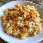 Close-up of a white bowl filled with creamy french onion butter rice topped generously with caramelized, crispy fried onions.