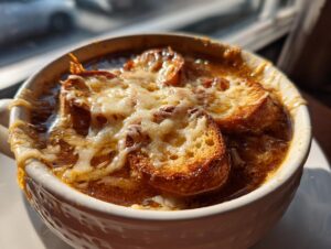 Close-up of a crock of rich french onion soup topped with toasted bread and bubbly, melted Gruyère cheese.