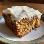 Close-up of a moist slice of applesauce cake topped with thick white cream cheese frosting.