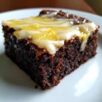 Close-up of a fudgy, dark chocolate Lemon Brownies square topped with a white glaze and bright yellow lemon zest.