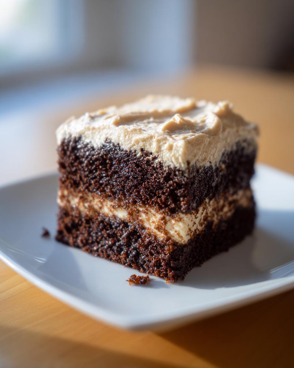 A square slice of dark, moist gingerbread cake layered and topped with light brown frosting, sitting on a white plate.