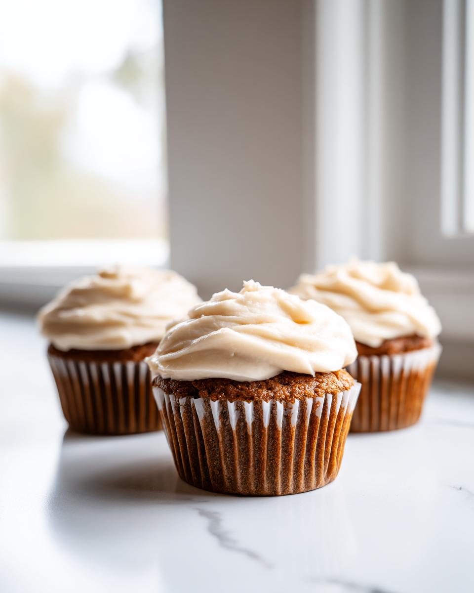 Three delicious gingerbread cupcakes topped with thick, creamy frosting sitting on a white marble surface.