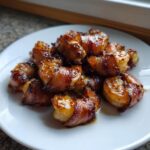 A pile of perfectly cooked, glazed bacon wrapped shrimp served on a white plate.