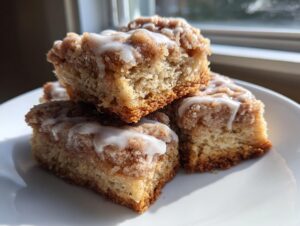 Close-up of three delicious coffee cake cookies stacked, featuring a cinnamon crumb topping and white glaze drizzle.