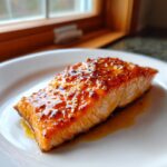 A perfectly cooked salmon fillet with a shiny, orange-colored glaze, served on a white plate.