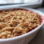 Close-up of a freshly baked rhubarb crisp with a golden, crunchy oat topping in a white baking dish.