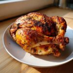 A beautifully roasted whole chicken with dark, seasoned, crispy skin resting on a white plate.