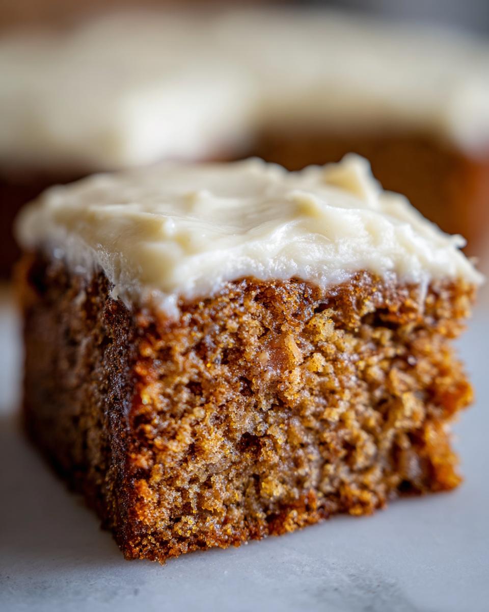 Close-up of a moist, spiced slice of applesauce cake topped with thick, white frosting.