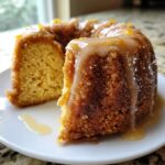 A close-up of a moist Bacardi Rum Cake slice on a white plate, heavily drizzled with a light brown rum glaze.