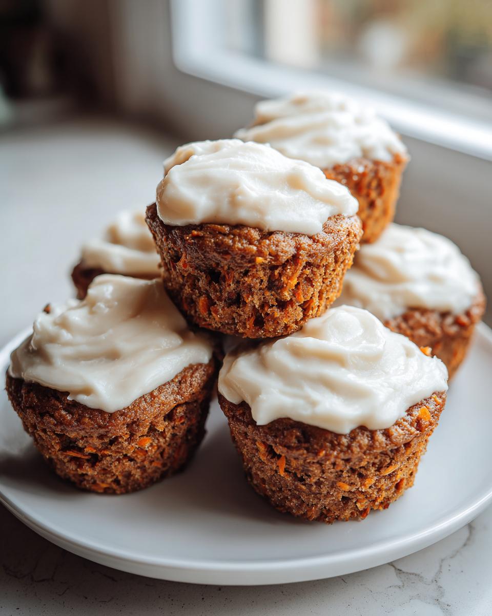 A stack of five moist carrot cake muffins topped with thick cream cheese frosting on a white plate.