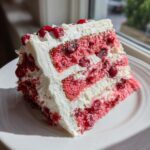 A tall slice of moist cherry cake featuring pink layers, whole cherries, and thick white frosting.