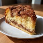 Close-up of a moist slice of sour cream coffee cake featuring a thick cinnamon streusel topping and layer.