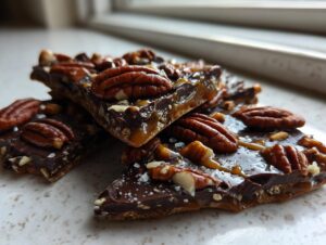 Close-up of broken pieces of rich Pecan Pie Bark topped with whole pecans, caramel drizzle, and sea salt.