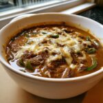Close-up of a hearty bowl of philly cheese steak soup topped with melted white cheese and green peppers.