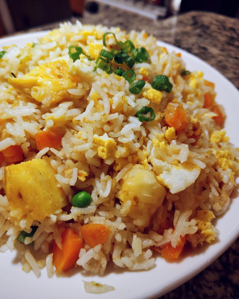 Close-up of a serving of delicious pineapple fried rice, featuring rice, scrambled egg, carrots, peas, and pineapple chunks, topped with green onions.