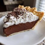 A perfect slice of french silk pie showing the rich chocolate filling, flaky crust, and whipped cream topped with chocolate shavings.