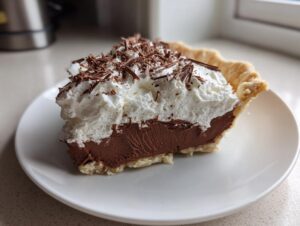 A generous slice of french silk pie showing rich chocolate filling, topped with whipped cream and chocolate shavings.