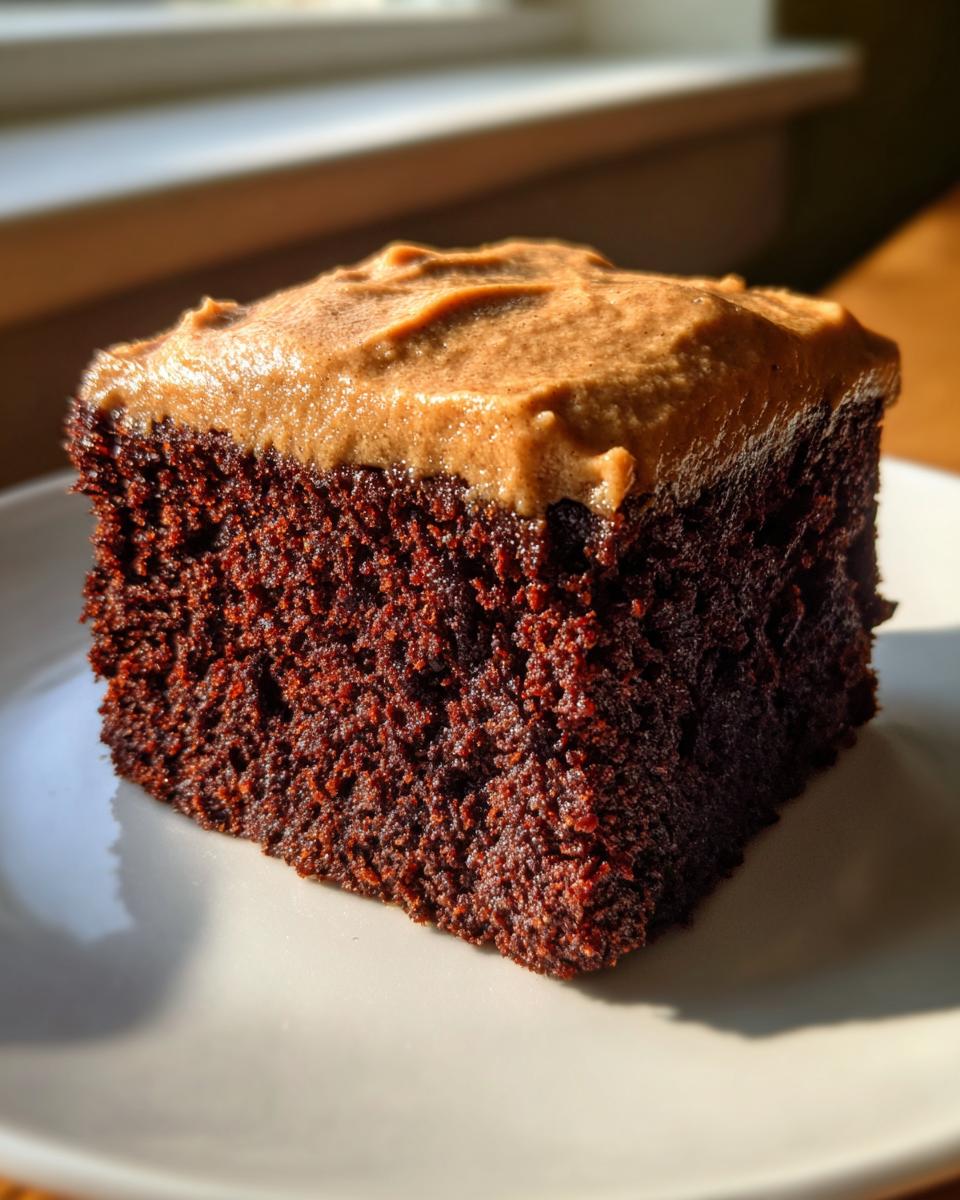 A rich, dark slice of gingerbread cake topped with thick brown frosting, sitting on a white plate.