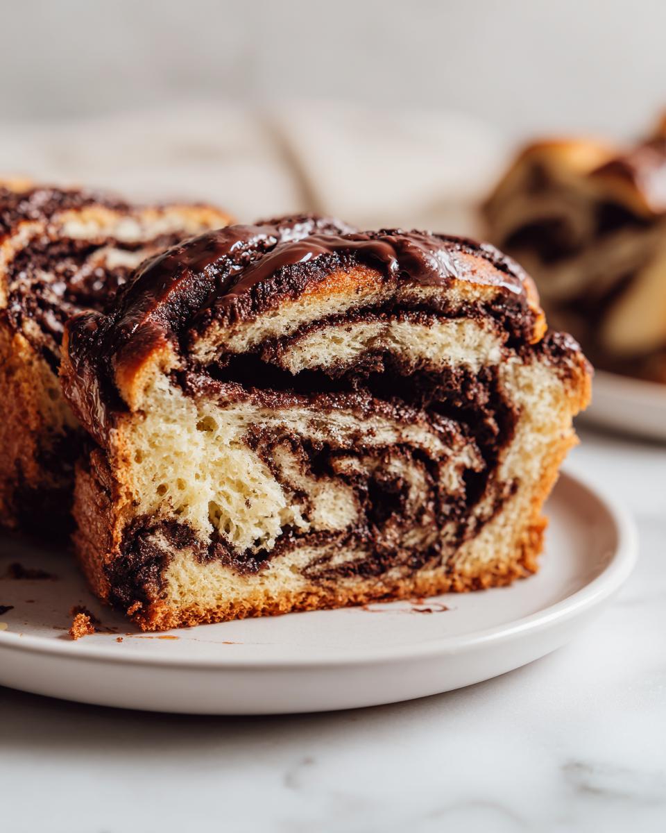Close-up of a thick slice of chocolate babka showing the rich, dark chocolate swirl pattern inside and glossy chocolate glaze on top.
