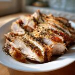 Close-up of perfectly cooked and sliced slow cooker turkey breast seasoned with herbs on a white plate.