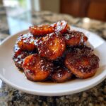 A close-up shot of thick slices of southern candied yams glistening with a rich, dark brown sugary glaze, piled on a white plate.
