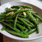 Close-up of bright green dilly beans tossed with chili flakes and sliced garlic in a white serving bowl.