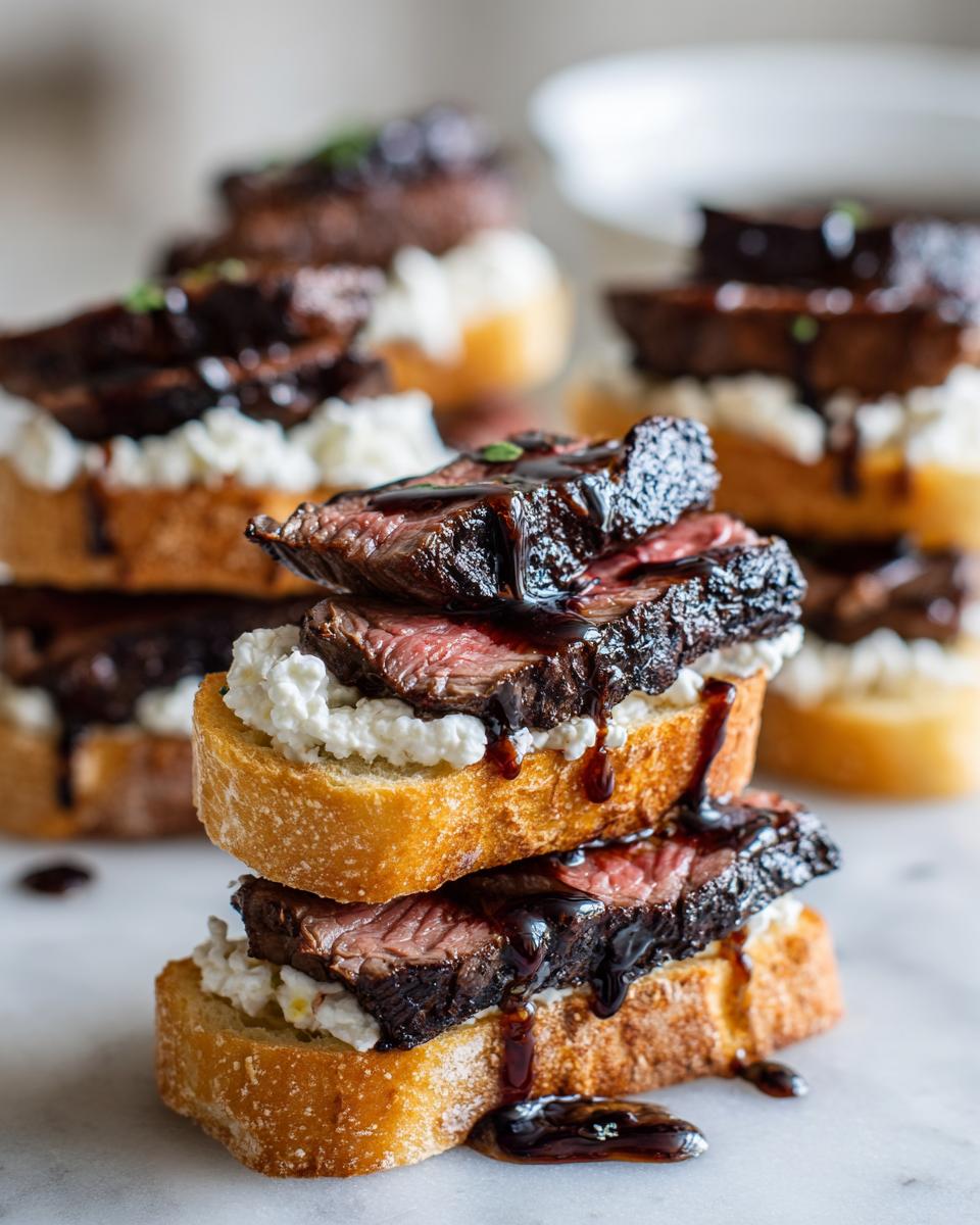 A stack of three steak crostini appetizers topped with creamy cheese and drizzled with a dark balsamic glaze.