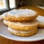 A stack of three golden sugar cookies topped with thick, white sugar cookie icing that hardens.