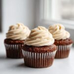 Three rich, dark gingerbread cupcakes topped with swirls of creamy, light-colored frosting.