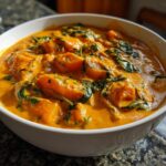Close-up of a vibrant orange vegan pumpkin curry with chunks of pumpkin and wilted spinach in a white bowl.