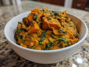 Close-up of a creamy, orange vegan pumpkin curry mixed with dark green spinach served in a white bowl.